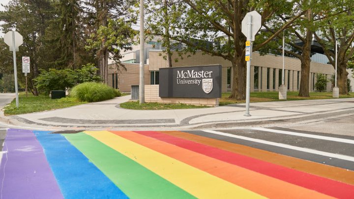 A painted crosswalk of the LGBTQIA+ pride flag on McMaster University's campus, across from the LR Wilson building.