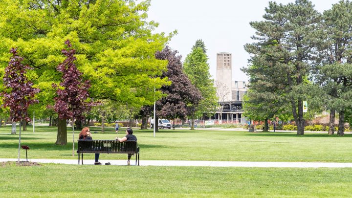 Two people sitting on a bench in he middle of the John Hopkins Engineering field on McMaster University's campus.