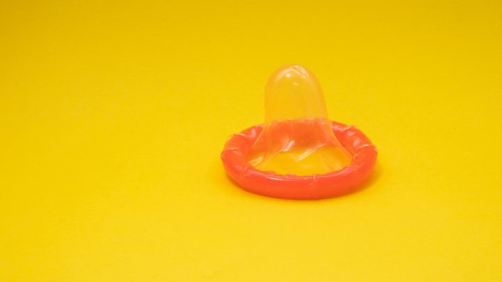 A red, unrolled condom on a yellow background