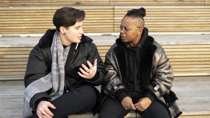 Two transmasculine people sitting together and having a serious conversation